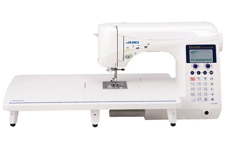 Front‑angle shot of the Juki HZL‑F600 quilting sewing machine: sleek white and blue body, large LCD display, wide built‑in extension table, knee‑lift lever visible, threading guides and presser foot with walking‑foot attachment, set against a neutral background.